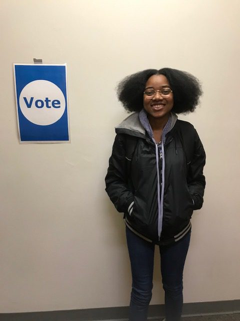 Tamara Morrison, Kalamazoo College Class of 2020 standing next to a sign that reads, "vote."