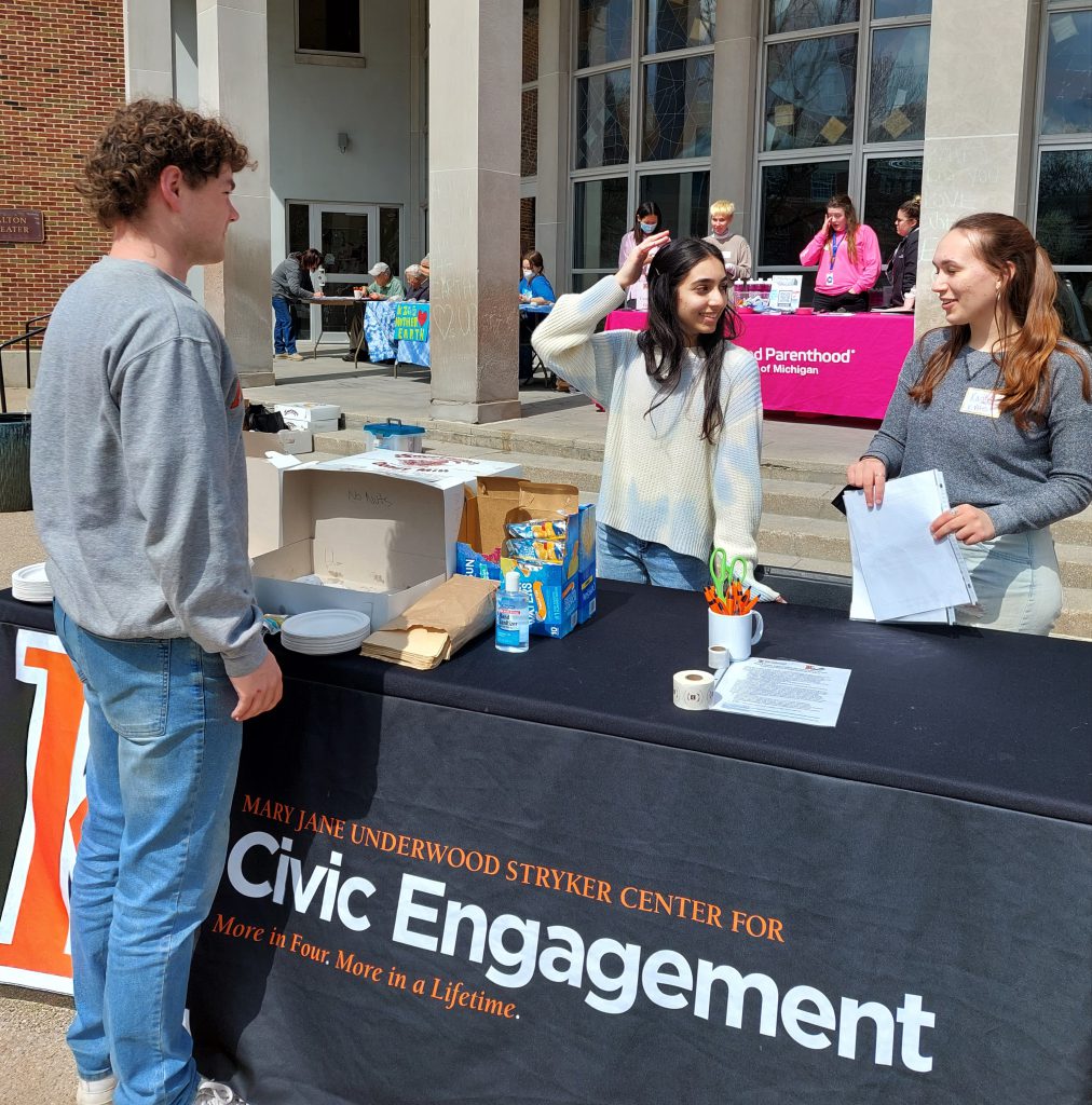 Three students talking while standing around a Center for Civic Engagement table at the 2022 K Votes Donuts and Democracy voter engagement fair.
